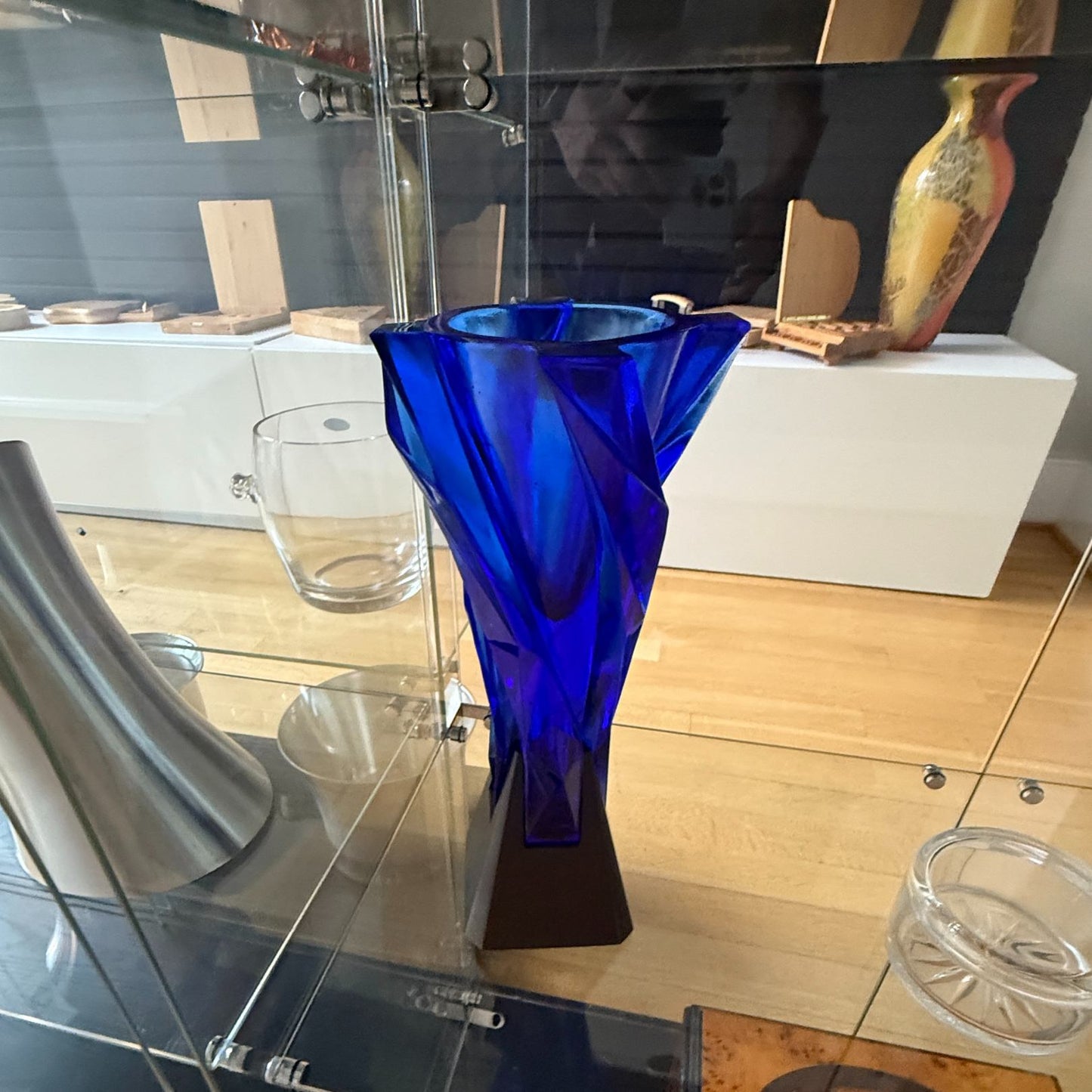 Blue glass vase on a glass shelf with a blurred background