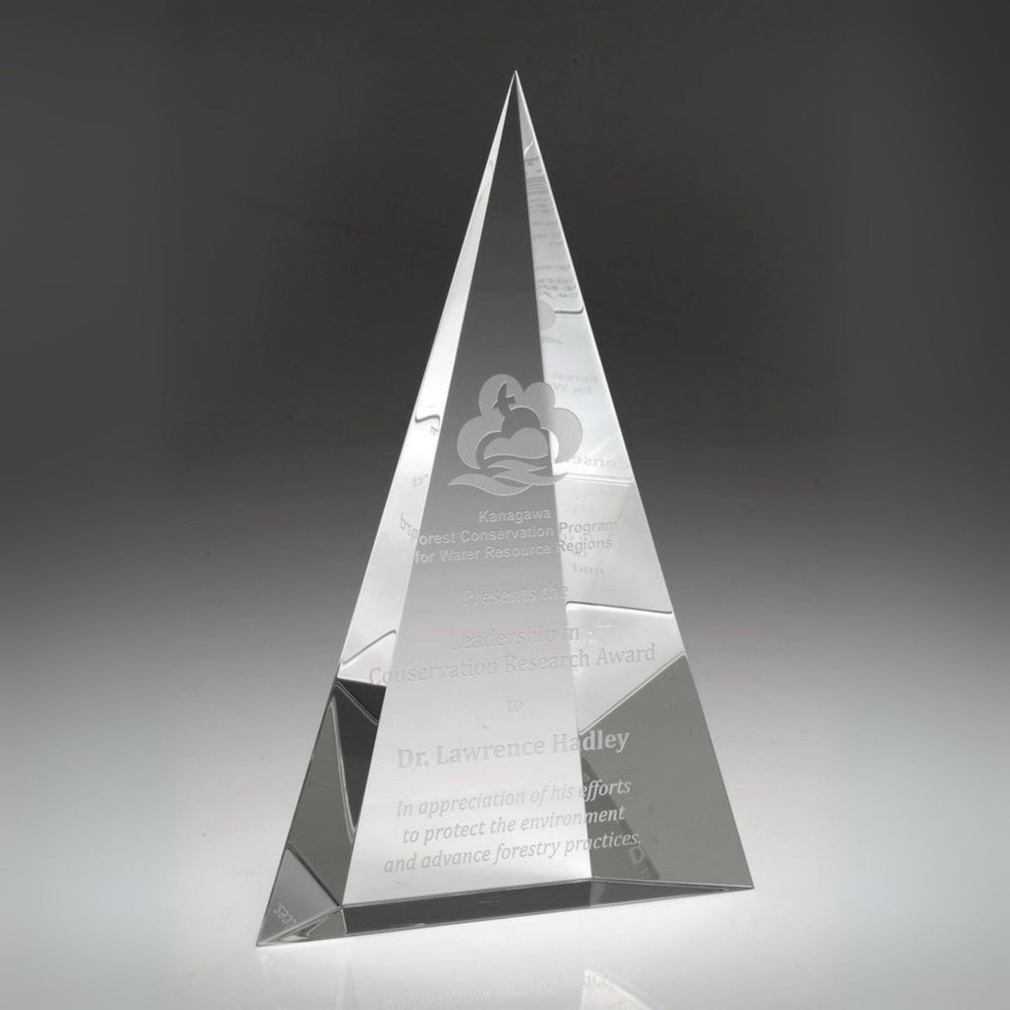 Crystal pyramid award with engraved text on a dark background