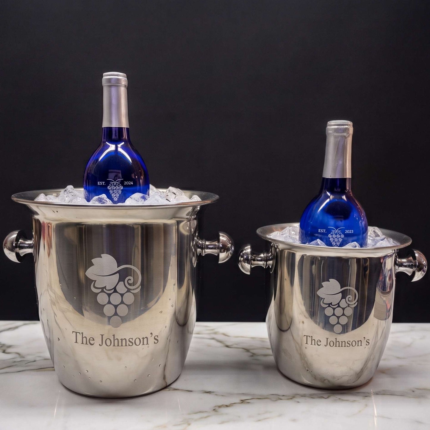 Two silver wine coolers with engraved logos and 'The Johnson's' text, containing blue bottles on a marble surface.