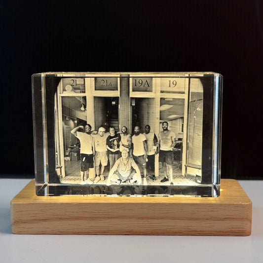 A custom rectangular clear crystal photo block displaying a black-and-white group photograph, mounted on a light-colored wooden base against a dark background.