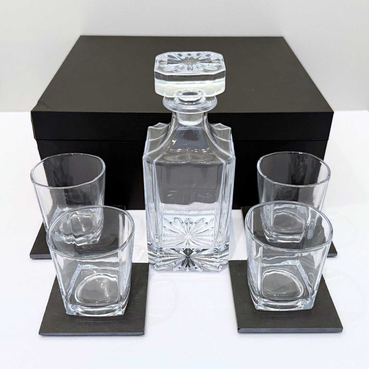 Crystal decanter set with four glasses on a white surface with a black box in the background.