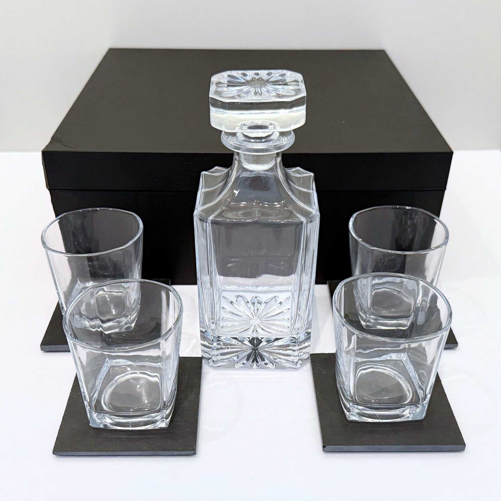 Crystal decanter set with four glasses on a white surface with a black box in the background.