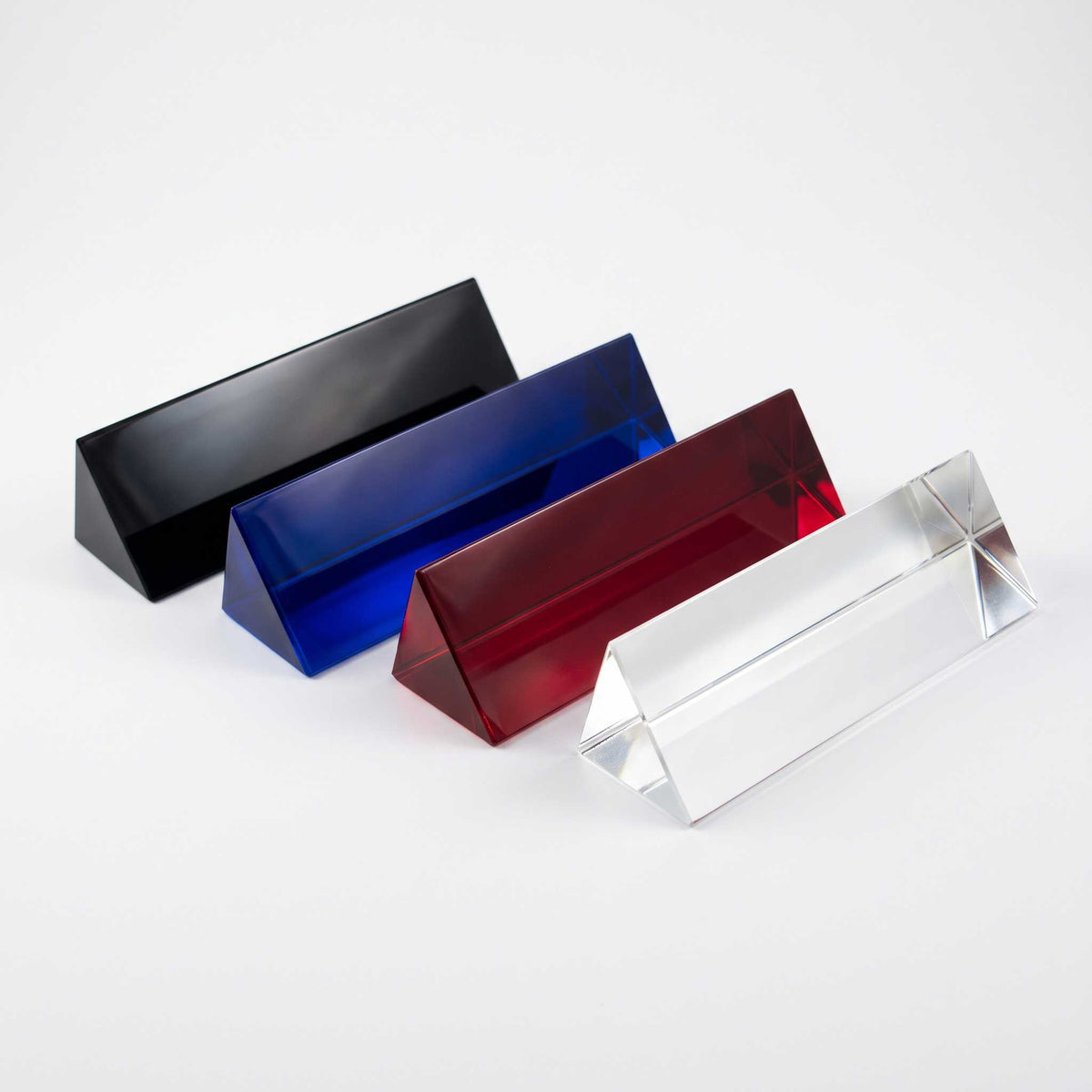 Four triangular crystal name plates in black, blue, red, and clear, arranged diagonally on a light gray background.
