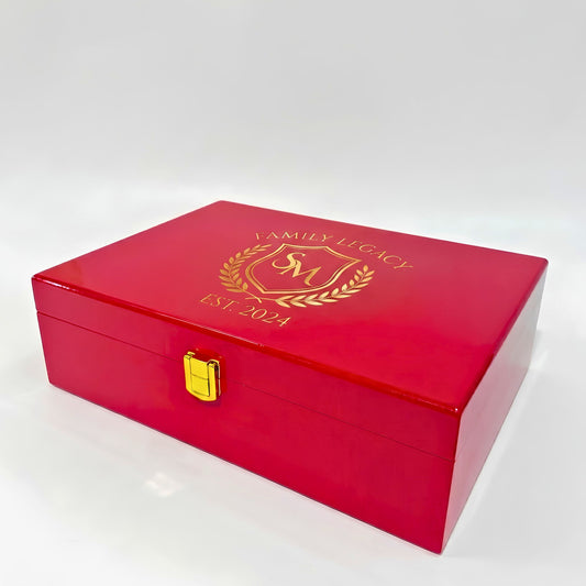 A glossy red wooden keepsake box with a gold clasp and a custom gold foil crest on the lid, set against a plain white background.