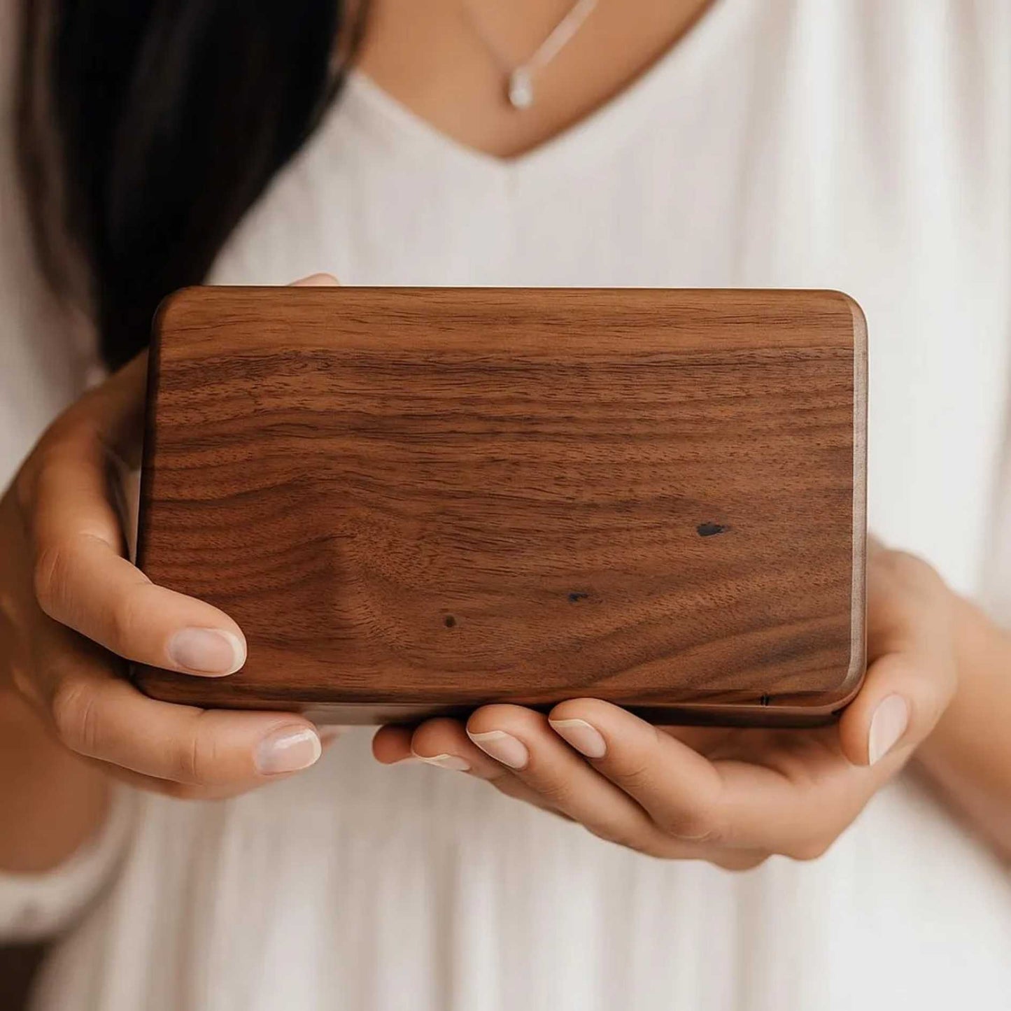 Wooden rectangular object held by hands against a neutral background