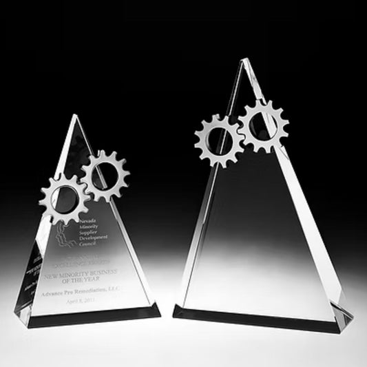 Two clear crystal triangular award trophies with interlocking gear accents, photographed on a black-to-white gradient studio background.