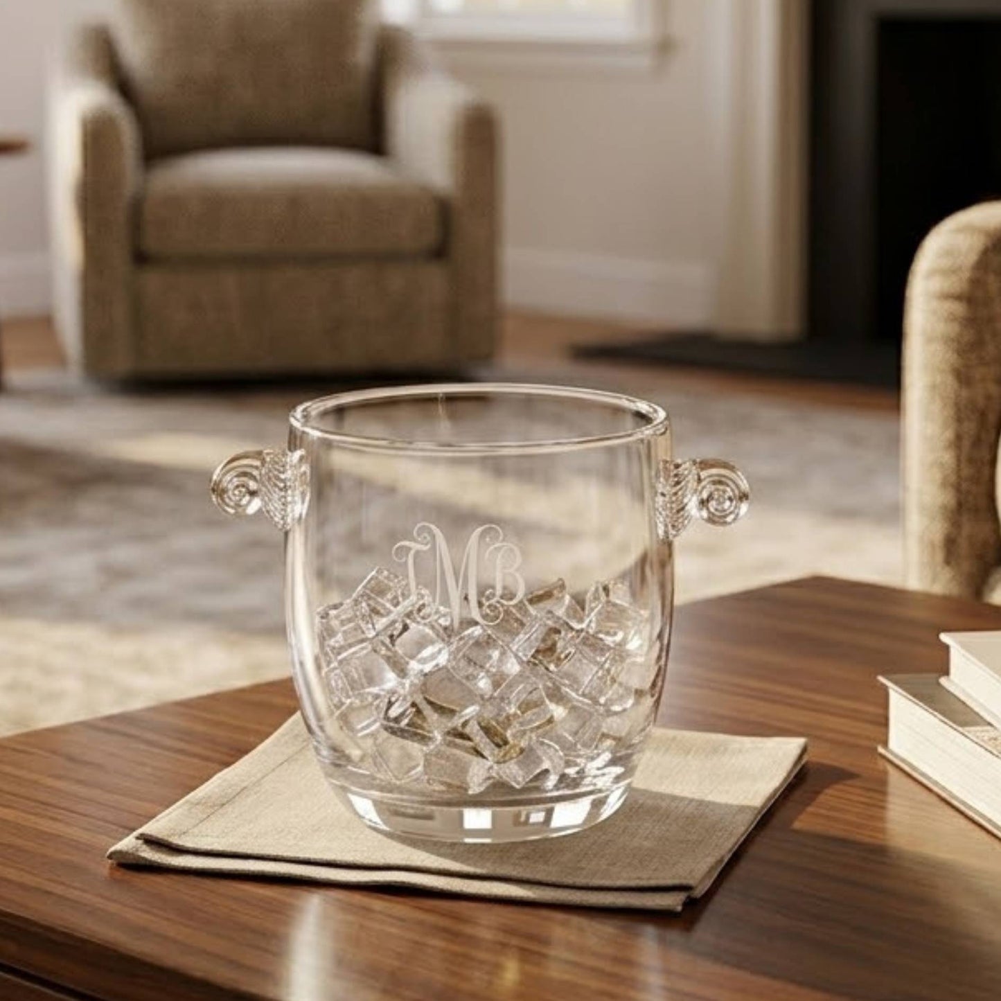 crystal ice bucket with curved handles engraved with monogram placed on living room table