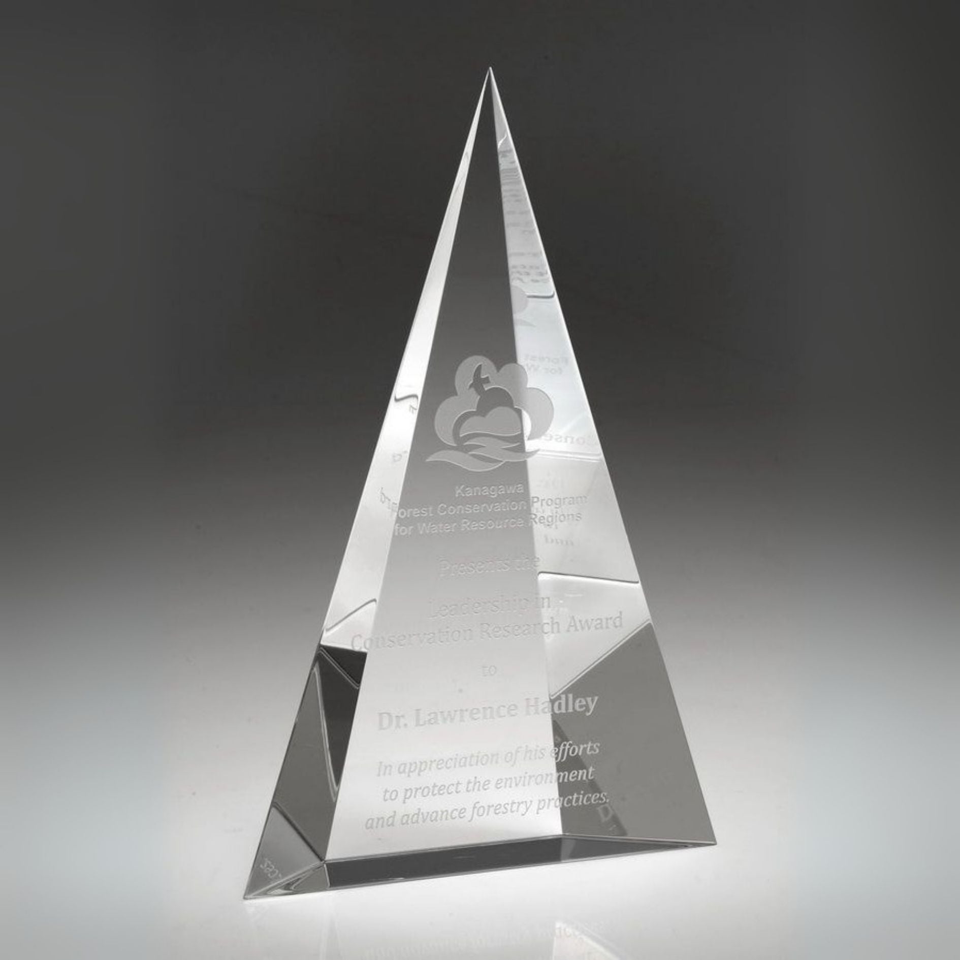 Crystal pyramid award with engraved text on a dark background