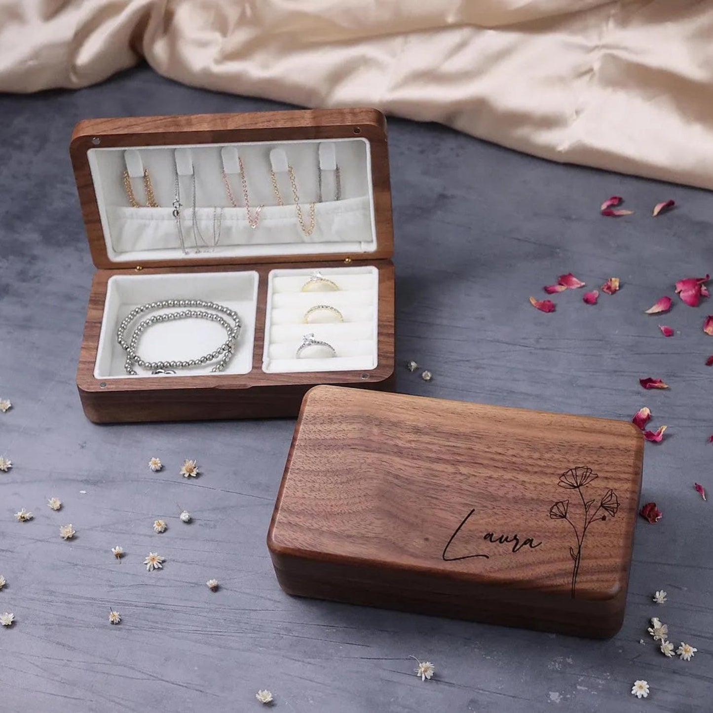 Wooden jewelry box with jewelry on a gray surface with flower petals.