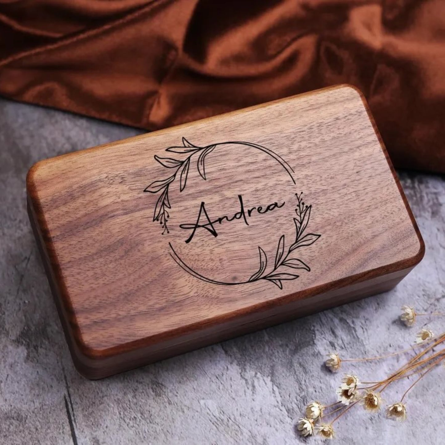 Wooden jewlelry box with engraved name 'Andrea' on a textured surface with a brown fabric background.
