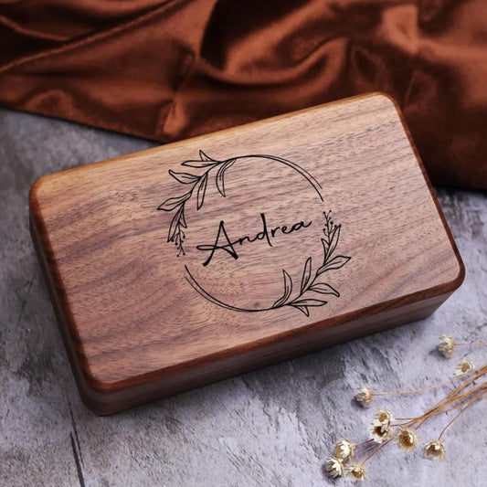 Wooden jewlelry box with engraved name 'Andrea' on a textured surface with a brown fabric background.