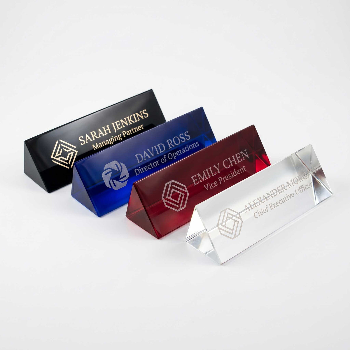 Four heavy crystal Name Plates shown in black, blue, red, and clear, arranged diagonally on a light gray background.