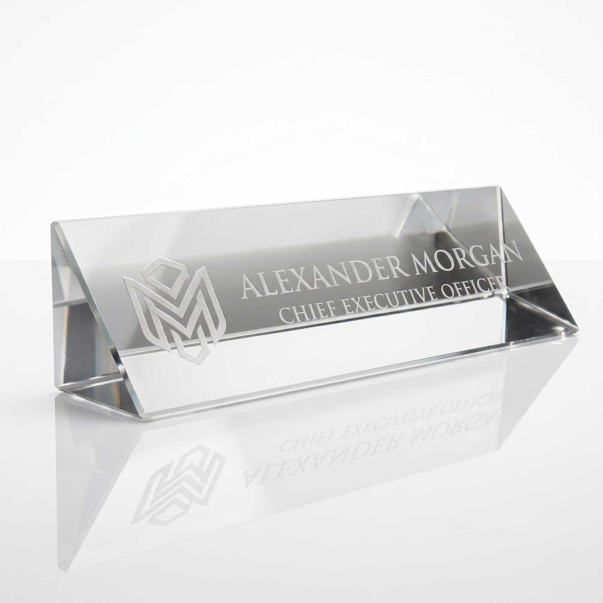 Crystal Name plate or glass business nameplate with laser-engraved text reading 'ALEXANDER MORGAN CHIEF EXECUTIVE OFFICE' and a geometric logo, shown on a clean white background with a soft reflection below.