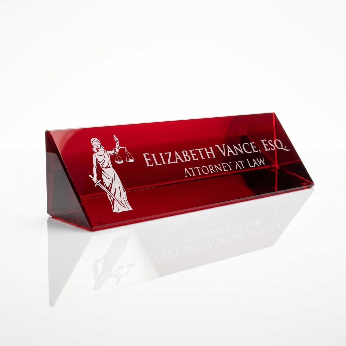 A red acrylic triangular desk nameplate with white laser-etched text reading 'Elizabeth Vance, Esq. Attorney at Law' and a white Lady Justice graphic, shown on a reflective white surface.