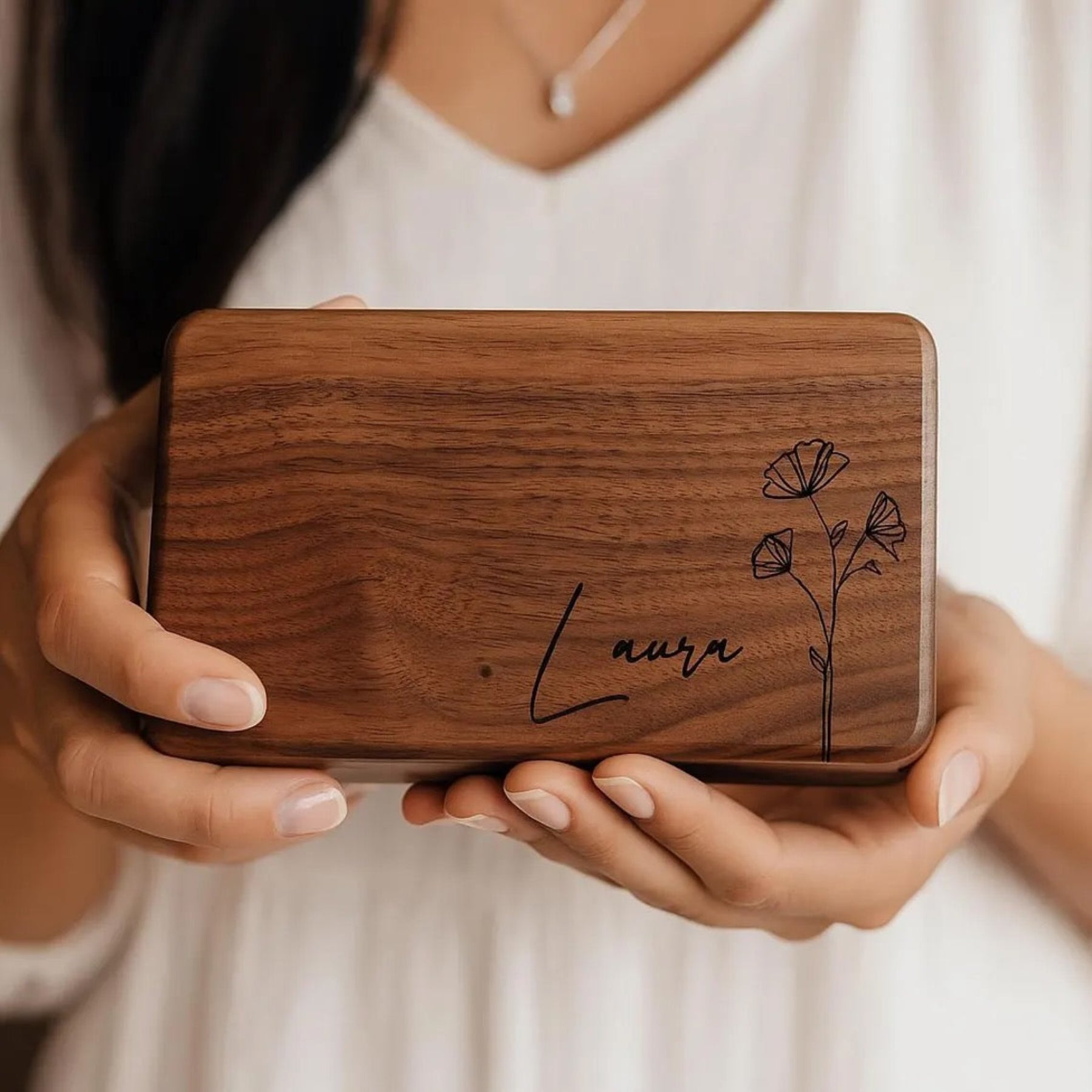Wooden box with engraved name and floral design held by a person