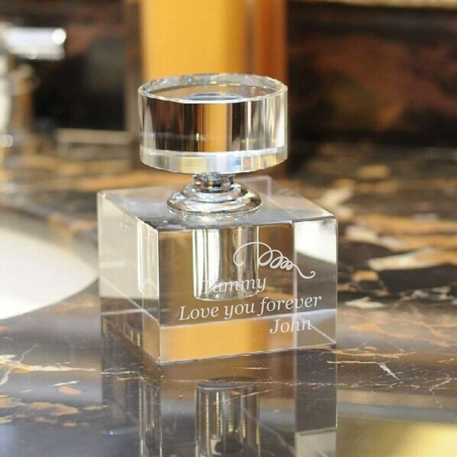 Clear glass perfume bottle with engraved text on a reflective surface