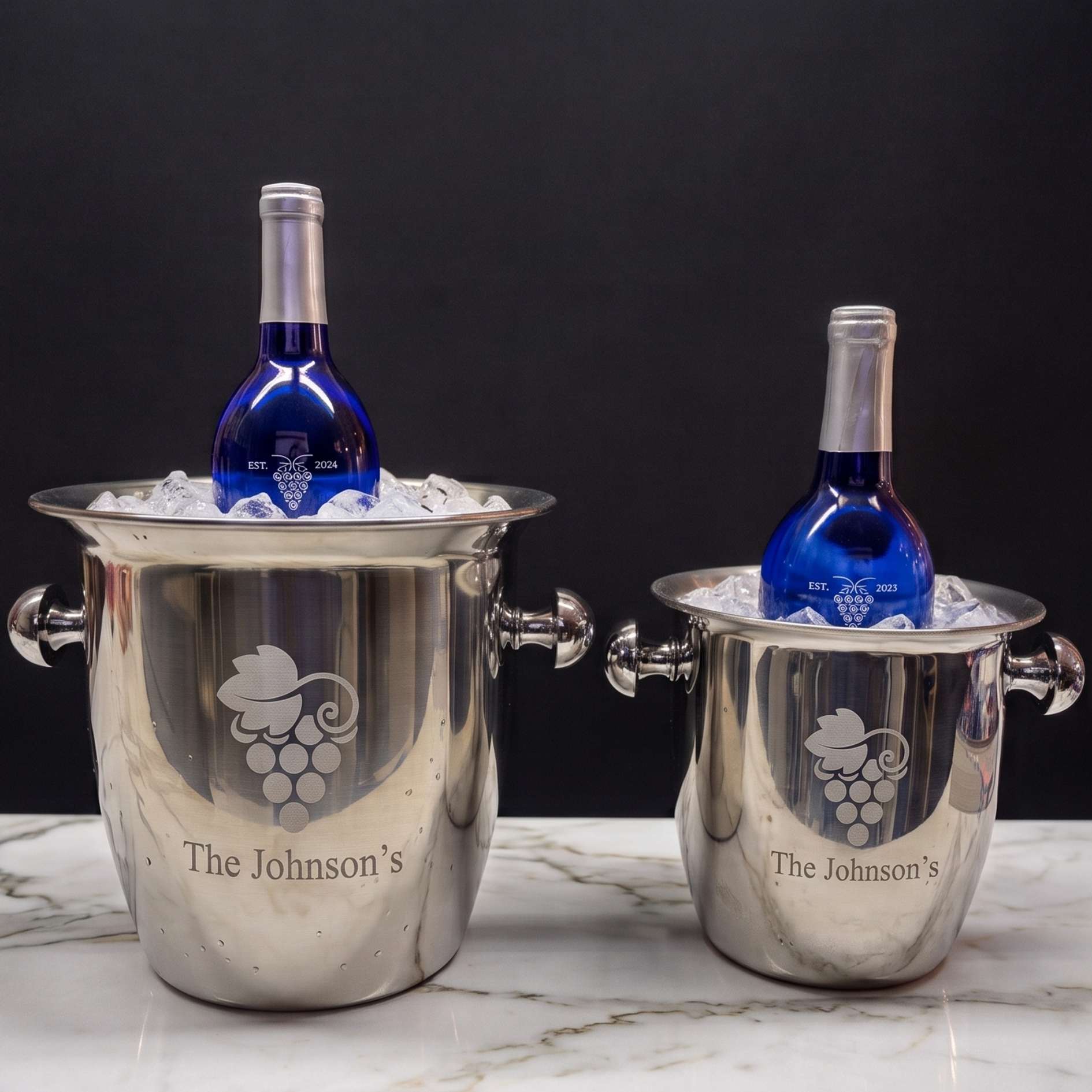 Two silver wine coolers with engraved logos and 'The Johnson's' text, containing blue bottles on a marble surface.